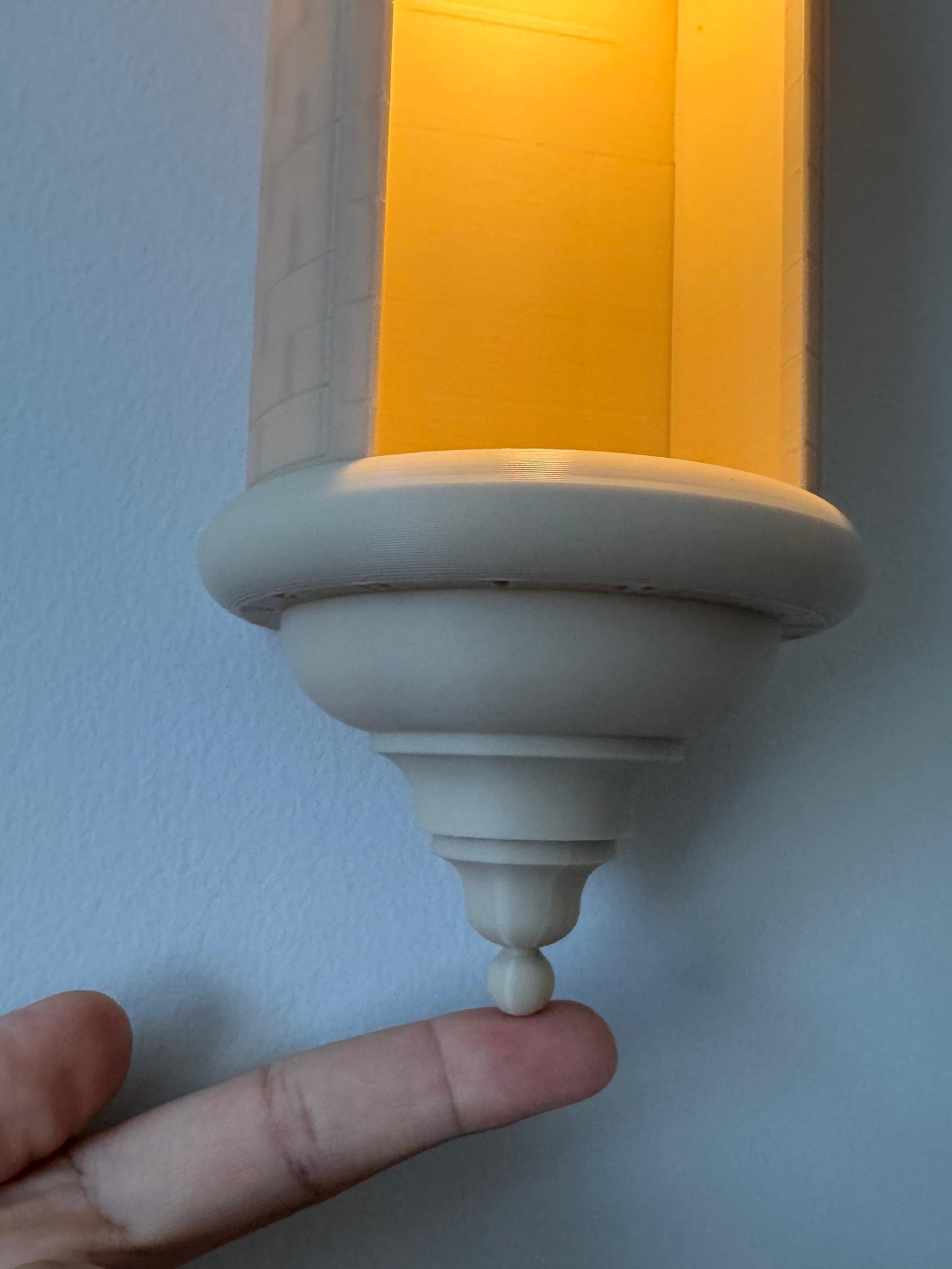 Decorative wall sconce with a hand pointing to it against a light blue wall.